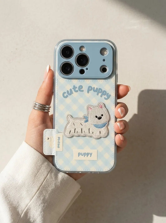 A close-up lifestyle shot of a hand holding CasePoppi The Gingham Bestie light blue puppy phone case under warm natural sunlight.