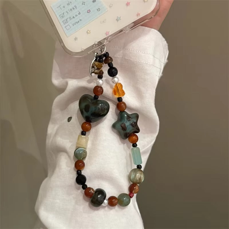 CasePoppi speckled ceramic beaded phone strap being held, complementing a white shirt, showing unique handmade aesthetic and glossy bead textures.
