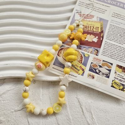 CasePoppi Cheese and Lemon Foodie beaded phone strap resting on a white wavy display surface next to a vintage food advertisement, showcasing the playful and colorful details of the charms.