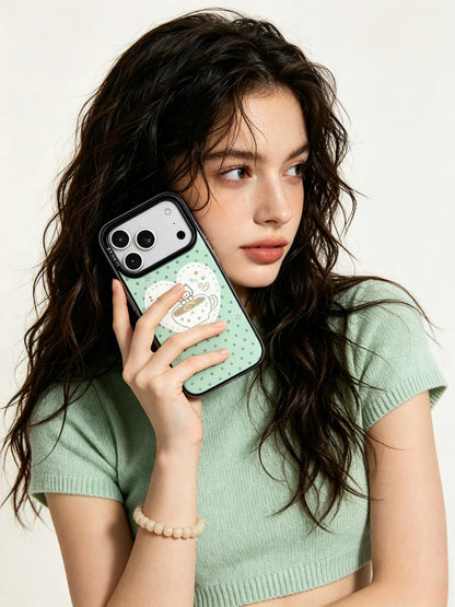 A close-up lifestyle photo of a young woman with wavy long dark hair, holding a mint green and white checkered phone case in a cozy minimalist indoor setting.