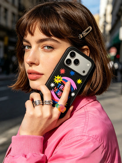 A stylish city street photography of a woman with a bob haircut wearing a pink denim jacket, holding a black phone case with colorful star and moon patterns.