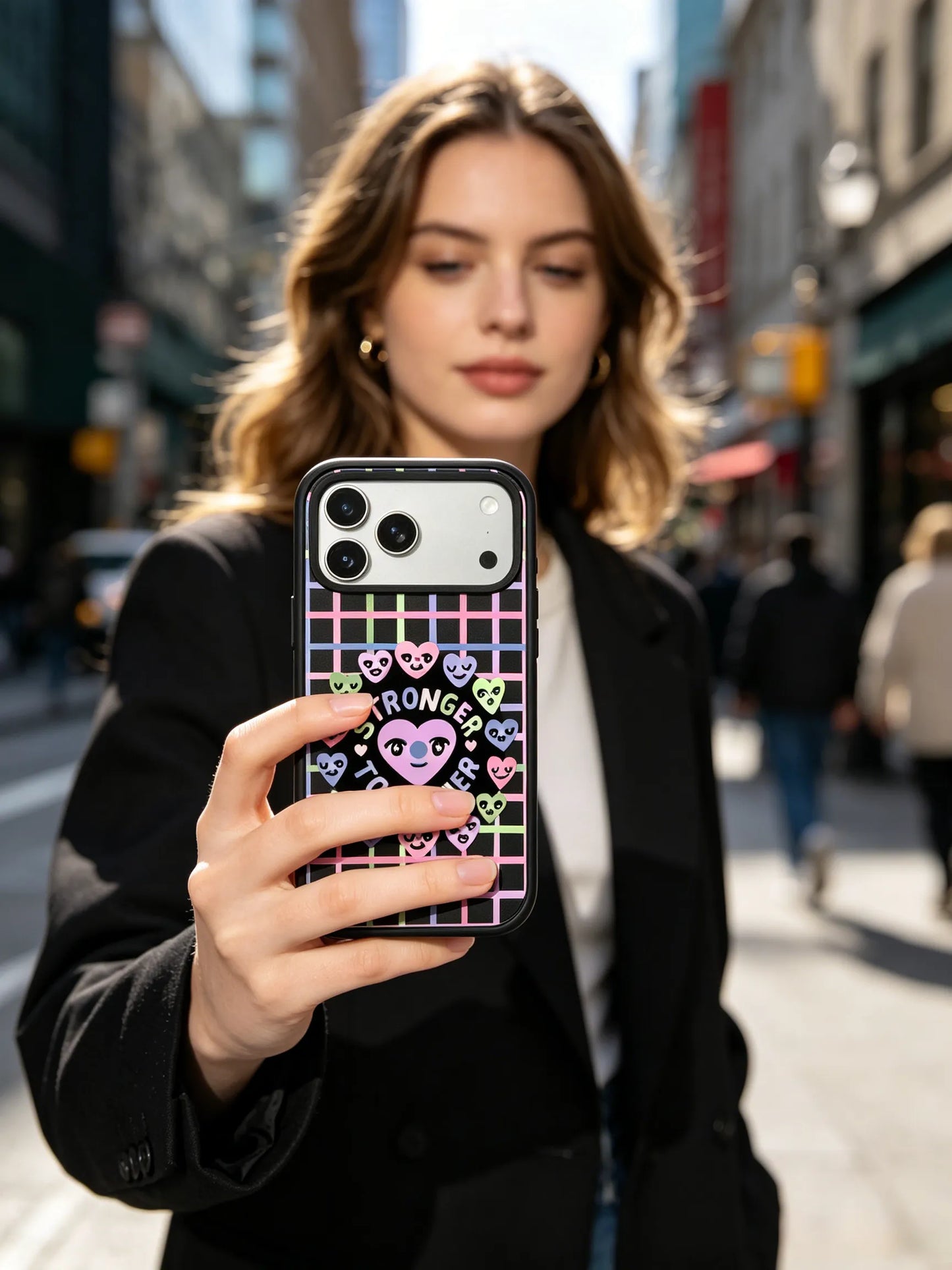 modern urban lifestyle photo of a young woman in a chic black blazer walking down a city street, displaying a purple heart checkered phone case.