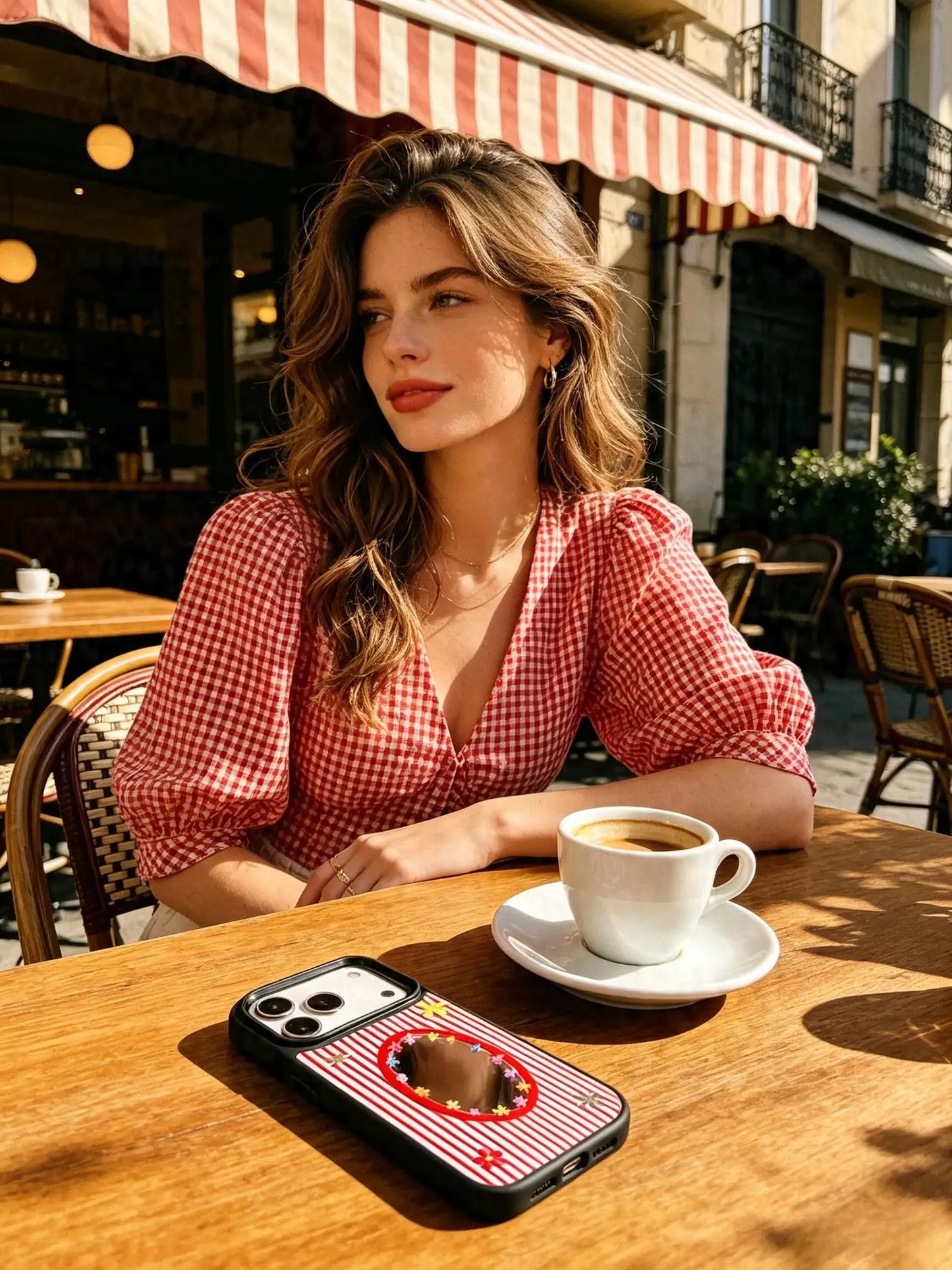 Woman holding red striped mirror phone case at cafe table
