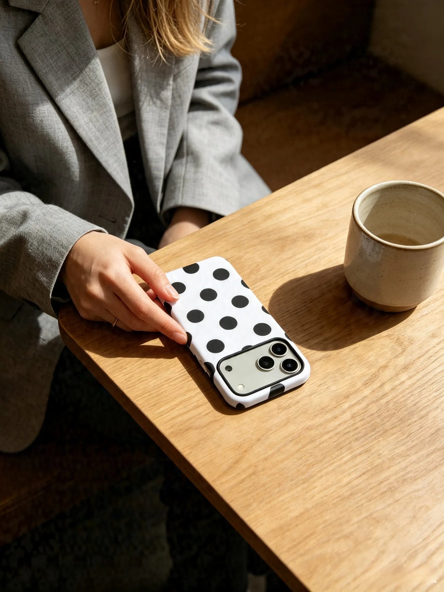 Hand holding white and black polka dot phone case on wooden table